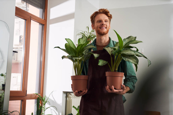 Florist in mask holding plants in pots - Zdjęcie, obraz