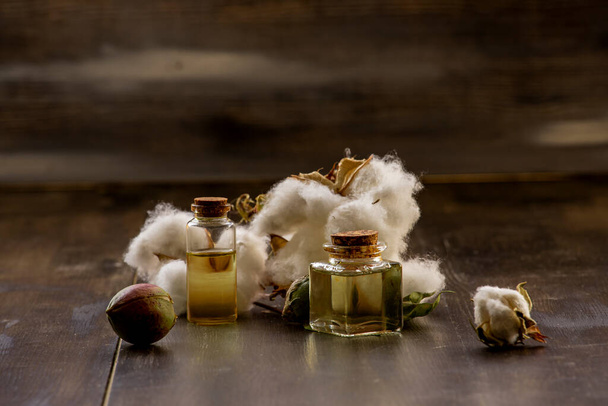 Bílé bavlny, zámotky a bavlníkový olej v láhvi na dřevěné podlaze. - Fotografie, Obrázek