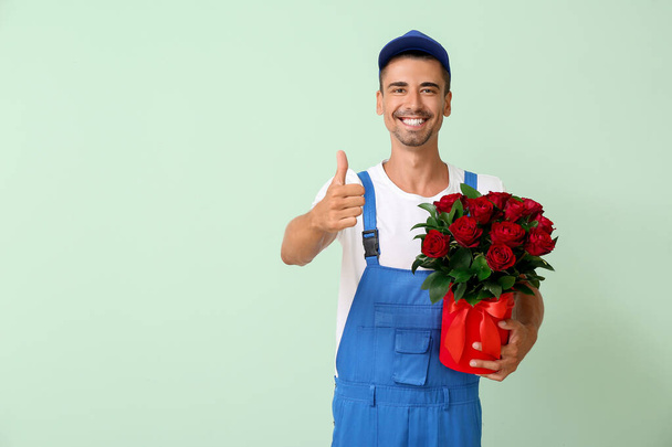 Delivery man with bouquet of flowers showing thumb-up on color background - Photo, Image