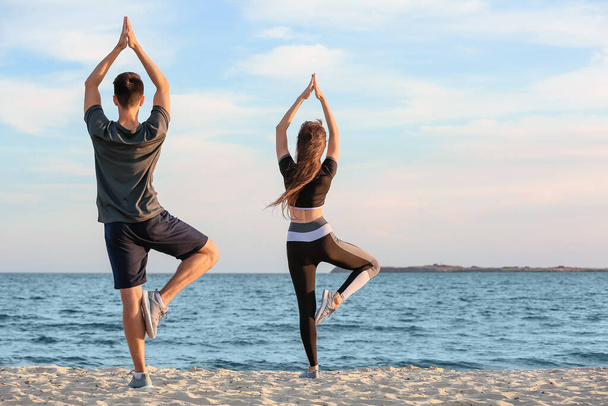 Sporty young couple practicing yoga on sea beach - Photo, Image