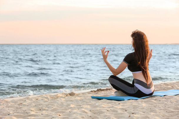 Sporty young woman practicing yoga on sea beach - Фото, изображение