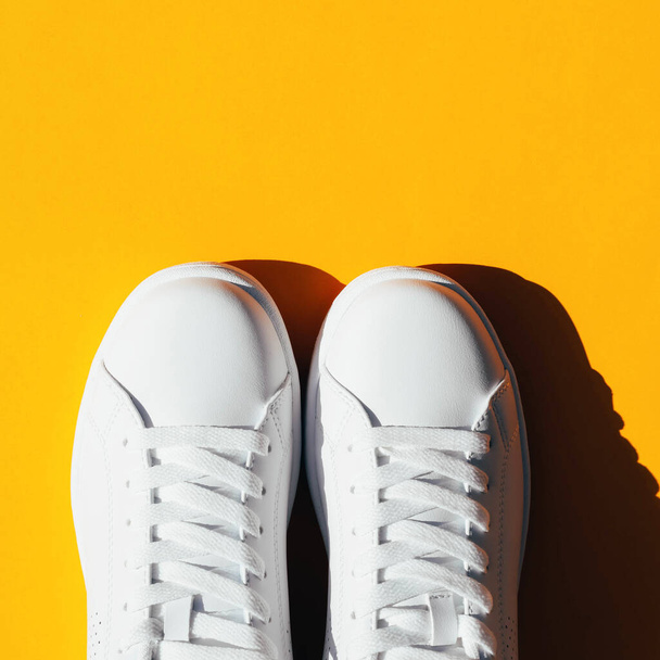 White sneakers on an orange background with hard shadows. Stylish sports shoes. - Photo, Image