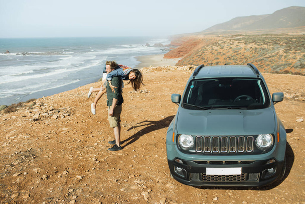 Car trip concept. Young and happy couple in love having fun and enjoying fantastic ocean view and coastline of Morocco. Wanderlust and lifestyle. - Photo, Image