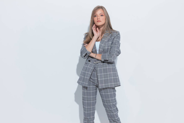 Confident fashion businesswoman holding hands on neck and wearing suit while standing on white studio background - Valokuva, kuva