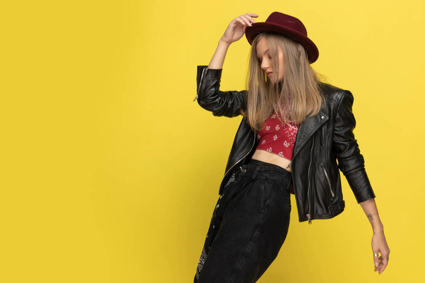 Confident fashion model taking off her hat and dancing on yellow studio background - Photo, Image