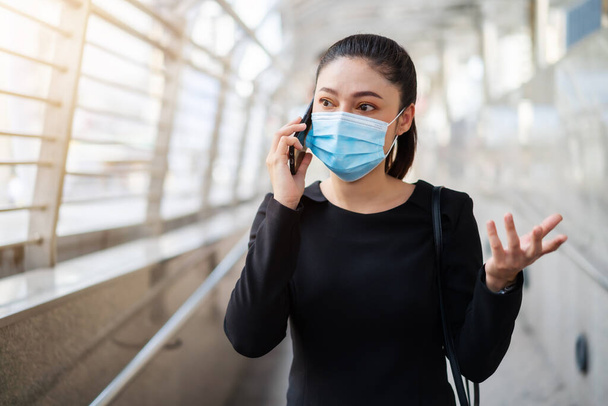 stressed woman wearing medical mask and talking with mobile phone about her business problem, protection from coronavirus (covid-19) pandemic - Fotó, kép
