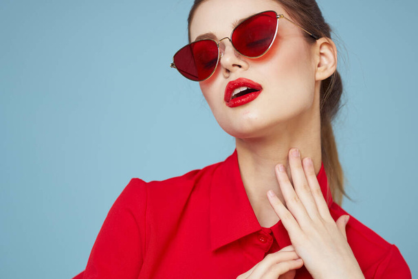 Beautiful woman in dark glasses red shirt bright makeup emotions attractive look blue background - Foto, imagen