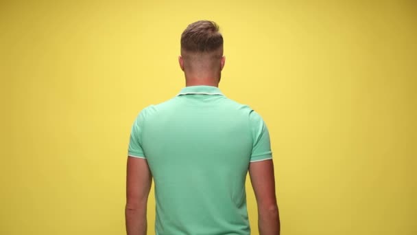 handsome casual man standing in rear view then turning around, crossing his arms and smiling on yellow background - Footage, Video