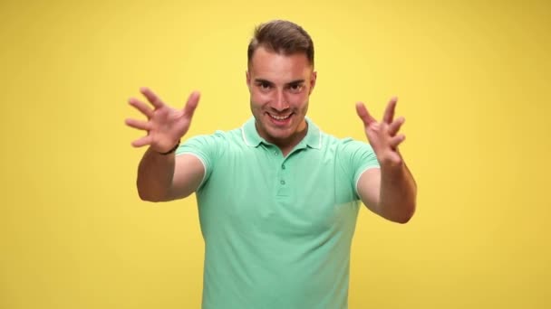 casual guy imitating slowly with his hands a big explosion, being happily surprised, pointing up and celebrating succes on yellow background - Footage, Video