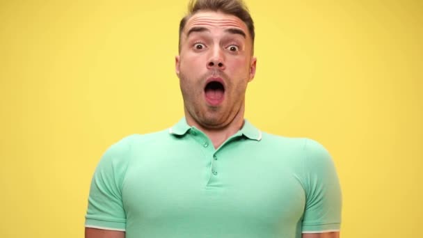 young casual man being shocked and leaning back, puffing cheeks and slapping his face on yellow background - Footage, Video