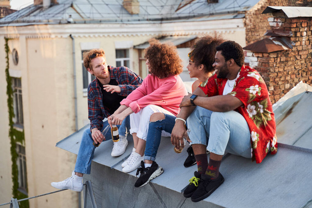 Young hipsters with beer chatting on urban roof - 写真・画像