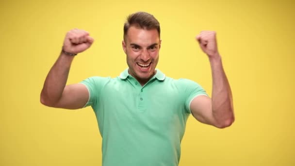 jonge casual man vieren succes, zwaaien met zijn vuisten in de lucht, dansen en ponsen op gele achtergrond - Video