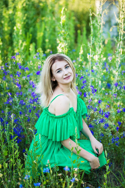 blond european girl in a green dress  on nature with blue flowers - Фото, изображение