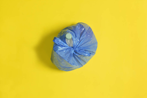 Draufsicht auf einen geschlossenen blauen Müllsack auf gelbem Hintergrund - Foto, Bild
