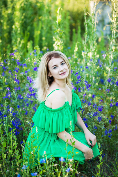 blond european girl in a green dress  on nature with blue flowers - Фото, изображение
