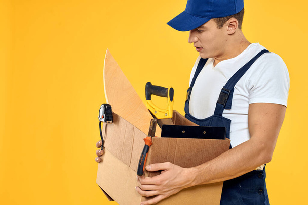 pracovník s krabicí v ruce nářadí nakladač žluté pozadí - Fotografie, Obrázek