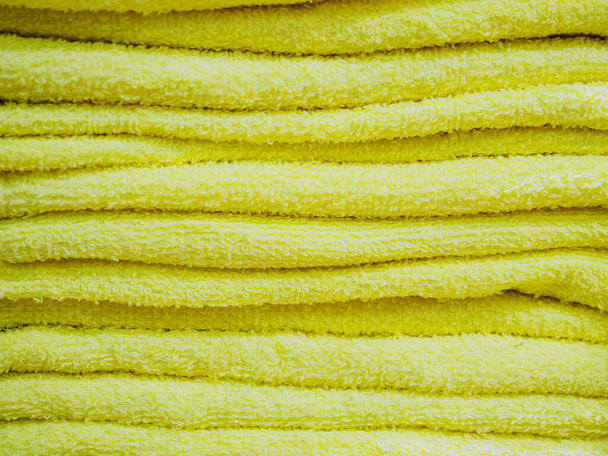 Las toallas amarillas iguales de rizo se apilan en una pila. Textura de fondo. Fotos a pantalla completa - Foto, imagen