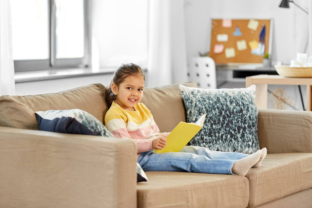 feliz sonriente niña leyendo libro en casa - Foto, imagen