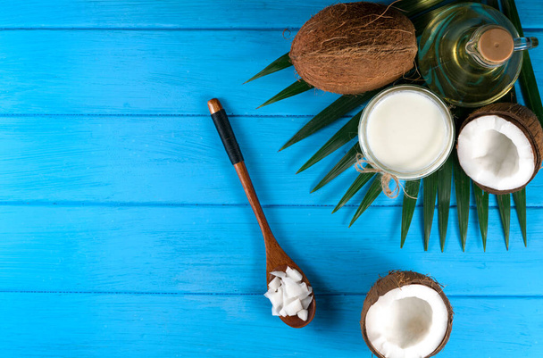Pieces of coconut in a wooden bowl with a spoon with coconut shavings and coconut oil on a blue background - Photo, Image