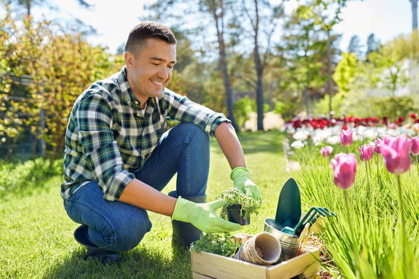 hombre feliz con herramientas en caja y flores en el jardín - Foto, Imagen