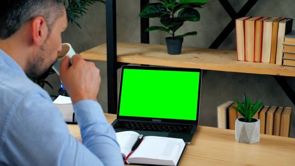オフィスのビジネスマンは、緑の画面のノートパソコンのコーヒーを飲むお茶に見えます - 写真・画像