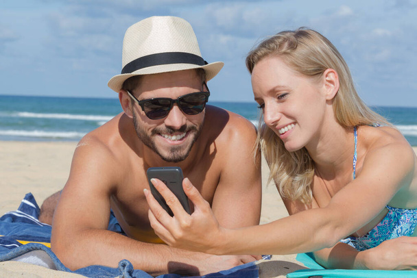 happy couple looking at mobile phone on the beach - Foto, imagen