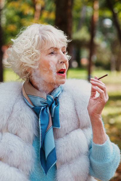 smutná módní starší žena s šedivými vlasy v kožichu venku kouření cigarety. Nezdravý životní styl, věk, stáří, závislost, koncepce špatných návyků. - Fotografie, Obrázek