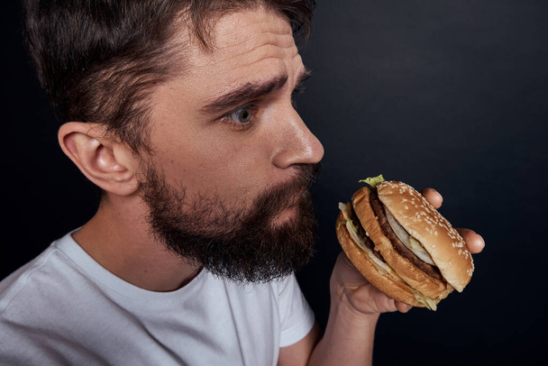 Hombre comiendo hamburguesa comida rápida restaurante Gourmet comer fondo oscuro - Foto, imagen