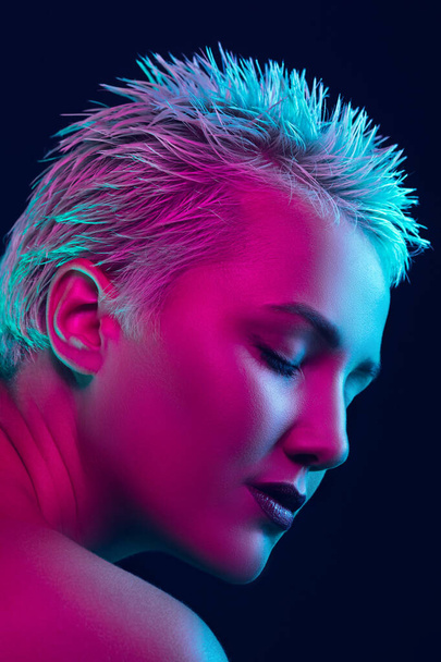 Portrait of female fashion model in neon light on dark studio background. - Фото, зображення