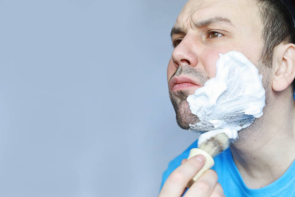Ένας άντρας ξυρίζεται μπροστά από έναν καθρέφτη. Αφρός ξυρίσματος. Ξυράφι μιας χρήσης. - Φωτογραφία, εικόνα