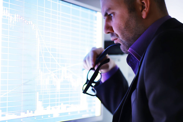 Een zakenman kijkt naar een grafiek op een monitor. Een wisselagent evalueert de ontwikkelingen op de beurs. Een man met een bril voor een curve van de dynamiek van de economie. - Foto, afbeelding