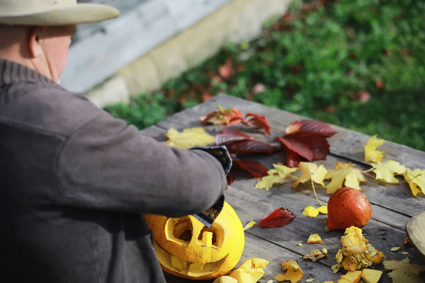 Traditions d'automne et préparatifs pour les vacances Halloween. Une maison dans la nature, une lampe faite de citrouilles est découpée à la table. - Photo, image