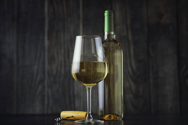 Transparent bottle of white dry wine on the table. White wine glass on a wooden wall background. - Foto, immagini