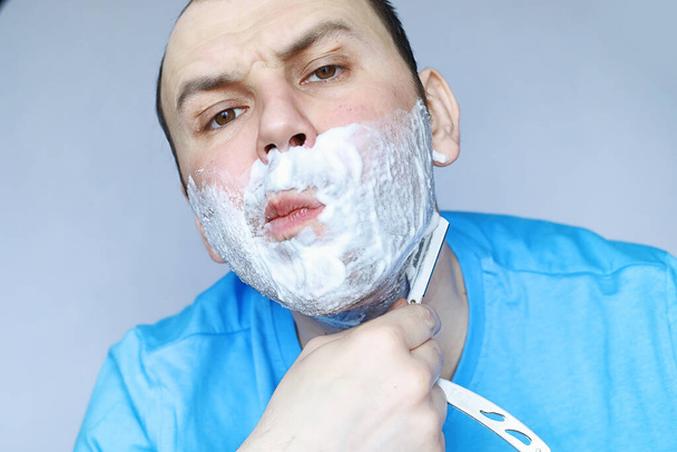 A man shaves in front of a mirror. Shaving foam. Disposable razor. - Photo, Image