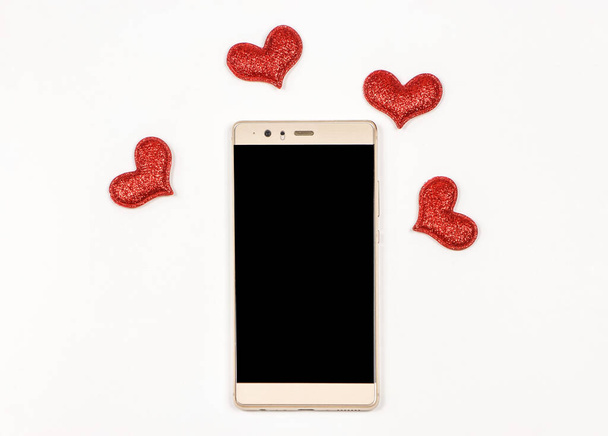 Vista superior o plano de pantalla en blanco teléfono móvil sobre fondo blanco decorado con corazones de purpurina roja y espacio de copia. día de San Valentín, comunicación, concepto de citas en línea. - Foto, imagen