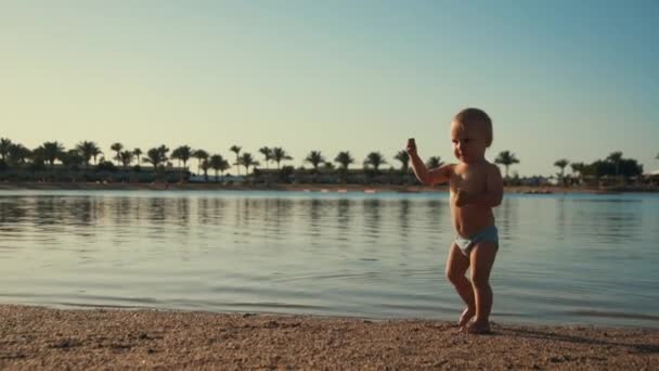 Uroczy chłopczyk cieszący się wakacjami na plaży. Aktywna zabawa dzieci na wybrzeżu. - Materiał filmowy, wideo