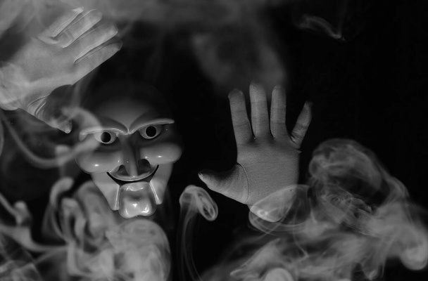 Máscara assustadora branca em um fundo preto com mãos brancas. - Foto, Imagem