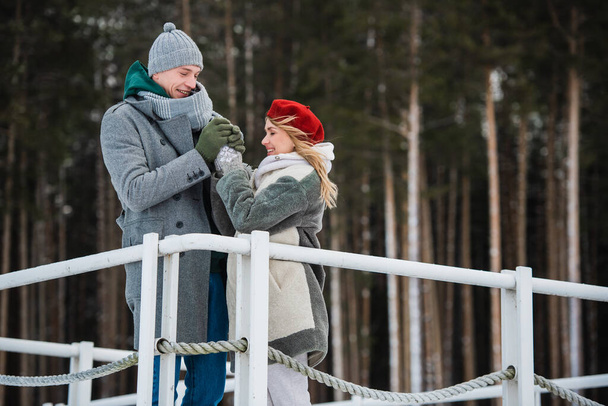 Winter walk of a couple in love in the woods, standing on the pier at the forest lake - Photo, Image
