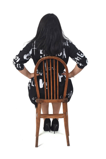  taustakuva latino nainen mekko ja korkokengät istuu tuolilla valkoisella taustalla, kädet lonkalla - Valokuva, kuva