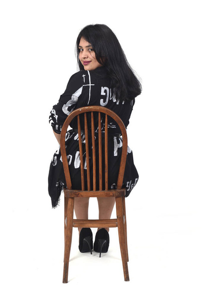  taustakuva latino nainen mekko ja korkokengät istuu tuolilla valkoisella taustalla, katsot kameraa - Valokuva, kuva