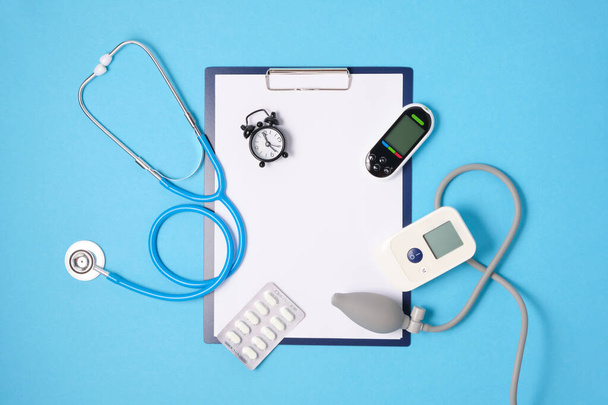 alarm clock, tonometer, glucose meter, clipboard and stethoscope on blue background place copy top view, measuring blood pressure and blood sugar level concept - Photo, Image