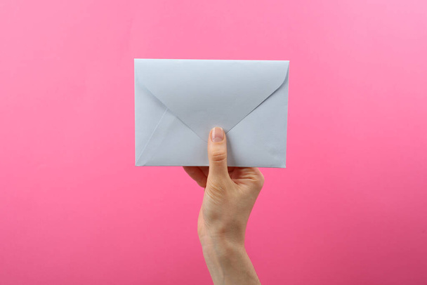 Woman holding white paper envelope on pink background, closeup - Foto, afbeelding