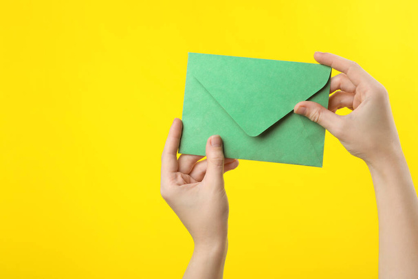 Woman holding green paper envelope on yellow background, closeup - Фото, зображення