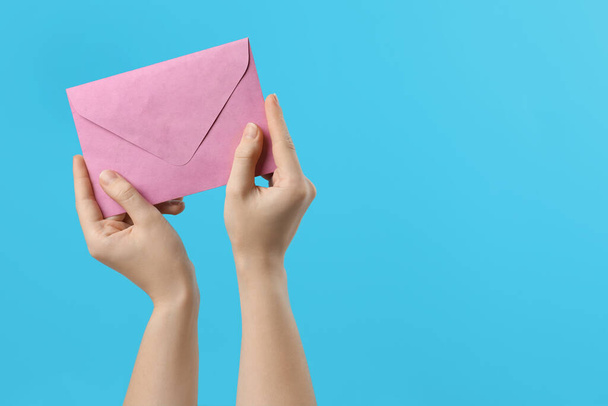 Woman holding pink paper envelope on light blue background, closeup. Space for text - Foto, imagen