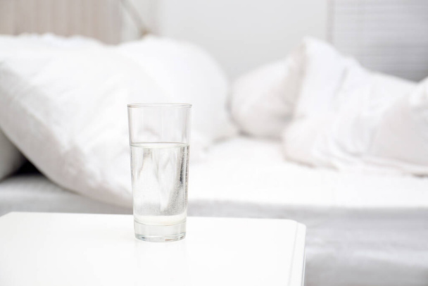 Glas water op wit nachtkastje in slaapkamer, ruimte voor tekst - Foto, afbeelding