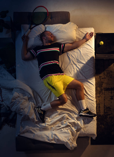 Top view of young professional tennis player sleeping at his bedroom in sportwear with racket - 写真・画像