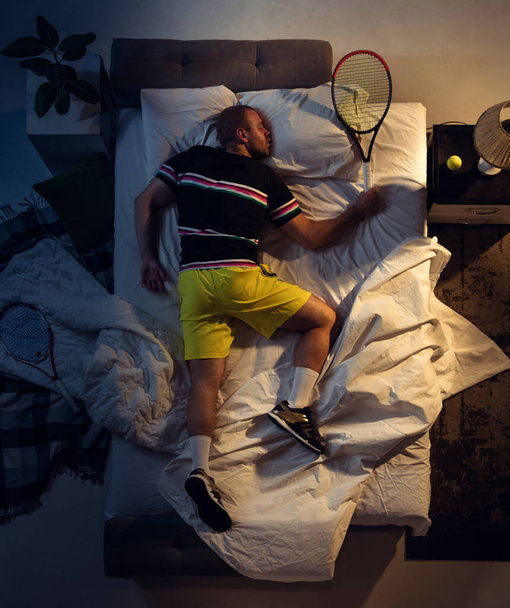 Top view of young professional tennis player sleeping at his bedroom in sportwear with racket - Foto, afbeelding