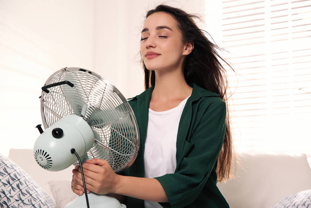 Woman with fan enjoying air flow at home. Summer heat - Foto, afbeelding