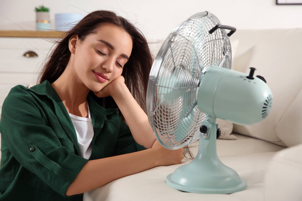 Woman enjoying air flow from fan at home. Summer heat - Foto, afbeelding