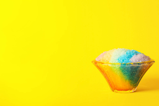 Rainbow shaving ice in glass dessert bowl on yellow background, space or text - Fotó, kép